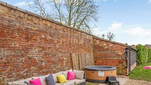 A cozy outdoor seating area with a brick wall, a hot tub, and a wicker sofa with cushions. - 3 bedroom accommodation in Tacolneston, near Wymondham (Tacolneston, near Wymondham)