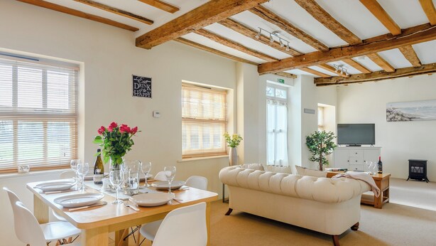 A dining area with a wooden table set for four, white chairs, and a sofa. - 3 bedroom accommodation in Tacolneston, near Wymondham (Tacolneston, near Wymondham)