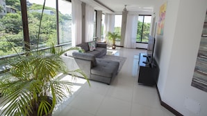 A modern living room with a grey sofa, a flat-screen TV, and a large window overlooking greenery. - El Cubil 8 (Sardinal)
