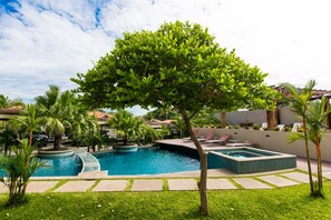 Una piscina con un árbol en el centro, rodeada de palmeras y sillas de descanso.