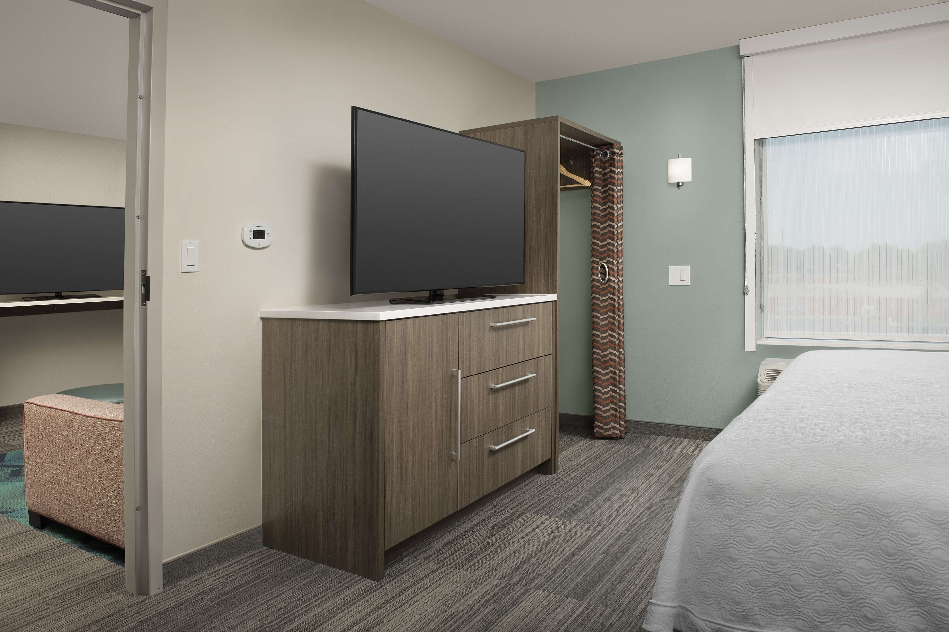 A hotel room with a bed, a TV on a dresser, a closet, and a window with curtains.