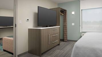 A hotel room with a bed, a TV on a dresser, a closet, and a window with curtains.
