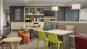 Un salon moderne avec un canapé, une table à manger et des chaises d’un vert vif. On y trouve également un coin cuisine avec une télévision et des étagères.