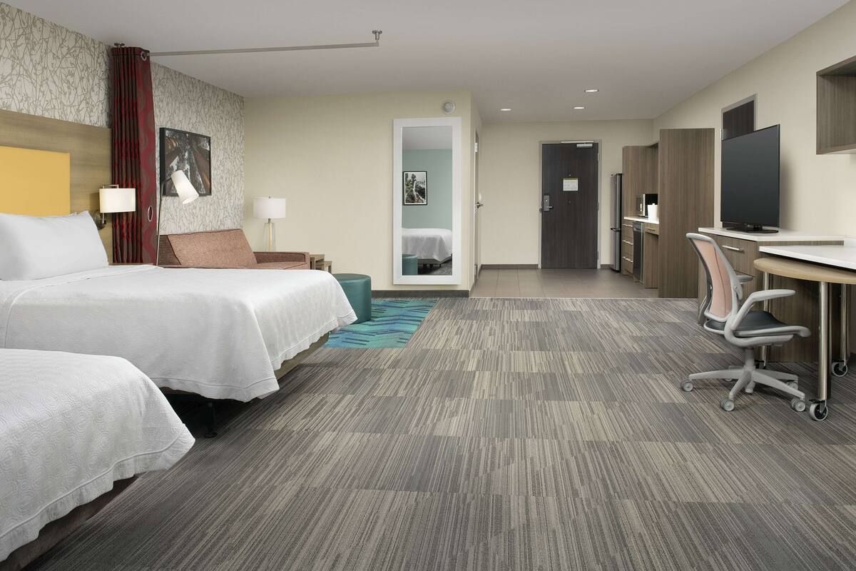 A hotel room with two beds, a desk, a television, and a bathroom visible through an open door.