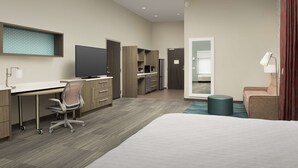 Une chambre d’hôtel équipée d’un lit, d’un bureau, d’une chaise, d’une télévision, d’une kitchenette et d’une salle de bain.