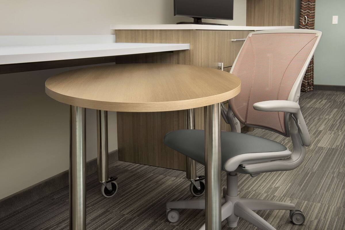 A modern office chair with wheels, a round table, and a flat-screen monitor on a desk.