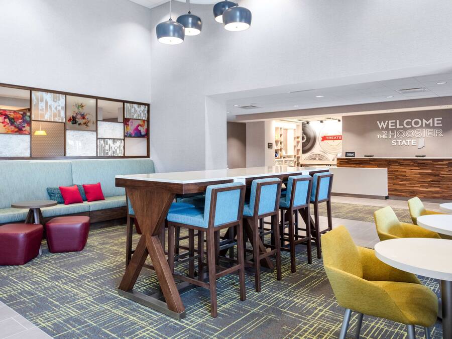 A modern hotel lobby with a reception desk, seating area, and a bar with stools.