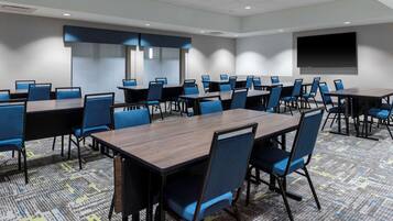 A conference room with multiple tables and chairs, a large screen, and a patterned carpet.