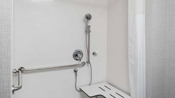A shower area with a grab bar, a handheld showerhead, and a shower seat.