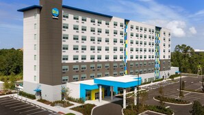 Ein modernes Hotel mit auffälligem 'tru'-Logo, einem Parkplatz und einer begrünten Eingangsbereich.