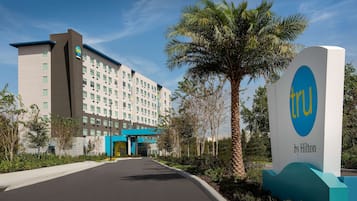 Entrada de un hotel con un cartel que dice "TRU by Hilton" y un edificio moderno de varios pisos y una entrada azul.
