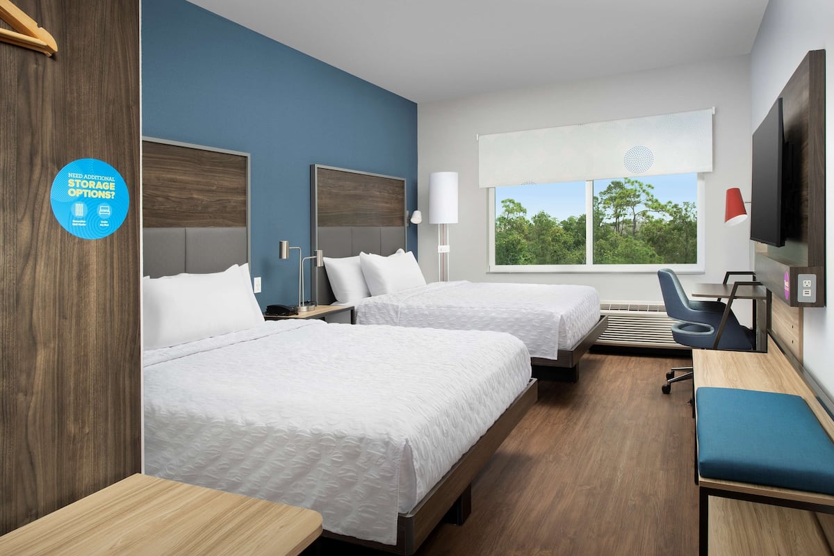 Habitación de hotel con dos camas, un escritorio, una silla, un televisor y una ventana con vistas a árboles.