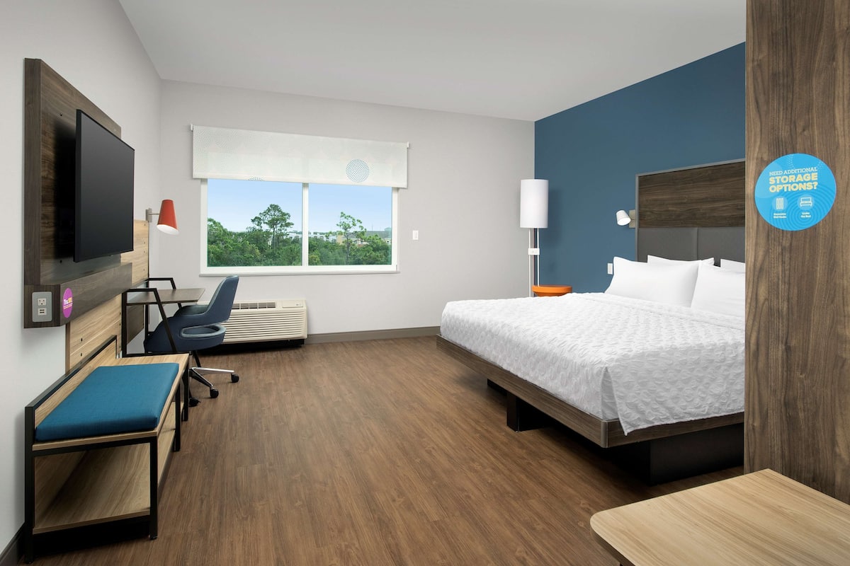Una habitación de hotel moderna con una cama, un escritorio, una silla, un televisor y una ventana con vistas a zonas verdes.