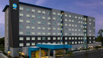 A modern hotel building with a prominent logo, multiple floors, and a parking lot.