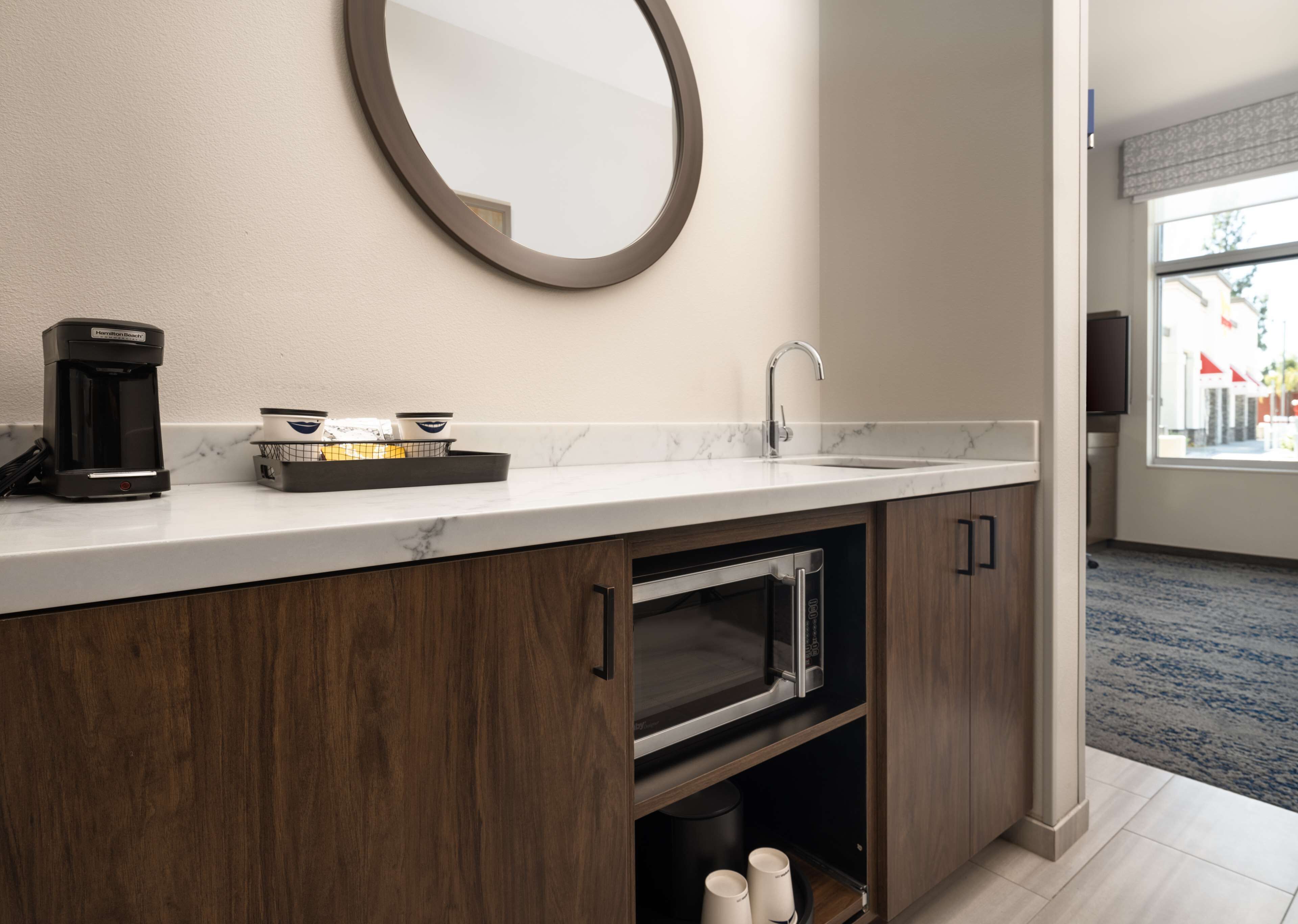 A modern bathroom with a marble countertop, a coffee maker, a sink, and a mirror.