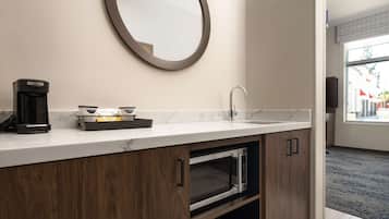 A modern bathroom with a marble countertop, a coffee maker, a sink, and a mirror.