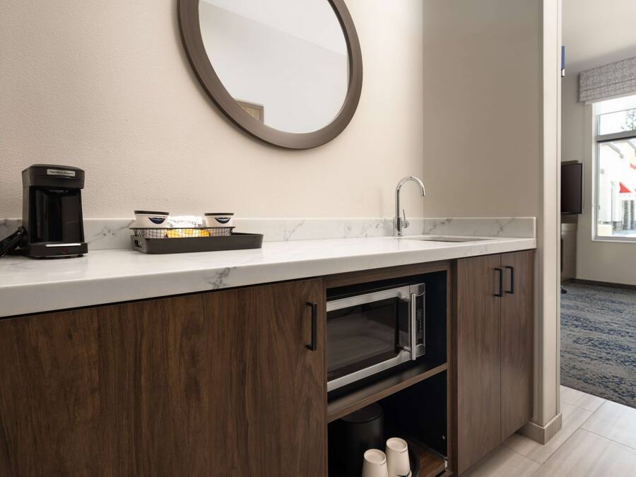 A modern bathroom with a marble countertop, a coffee maker, a sink, and a mirror.
