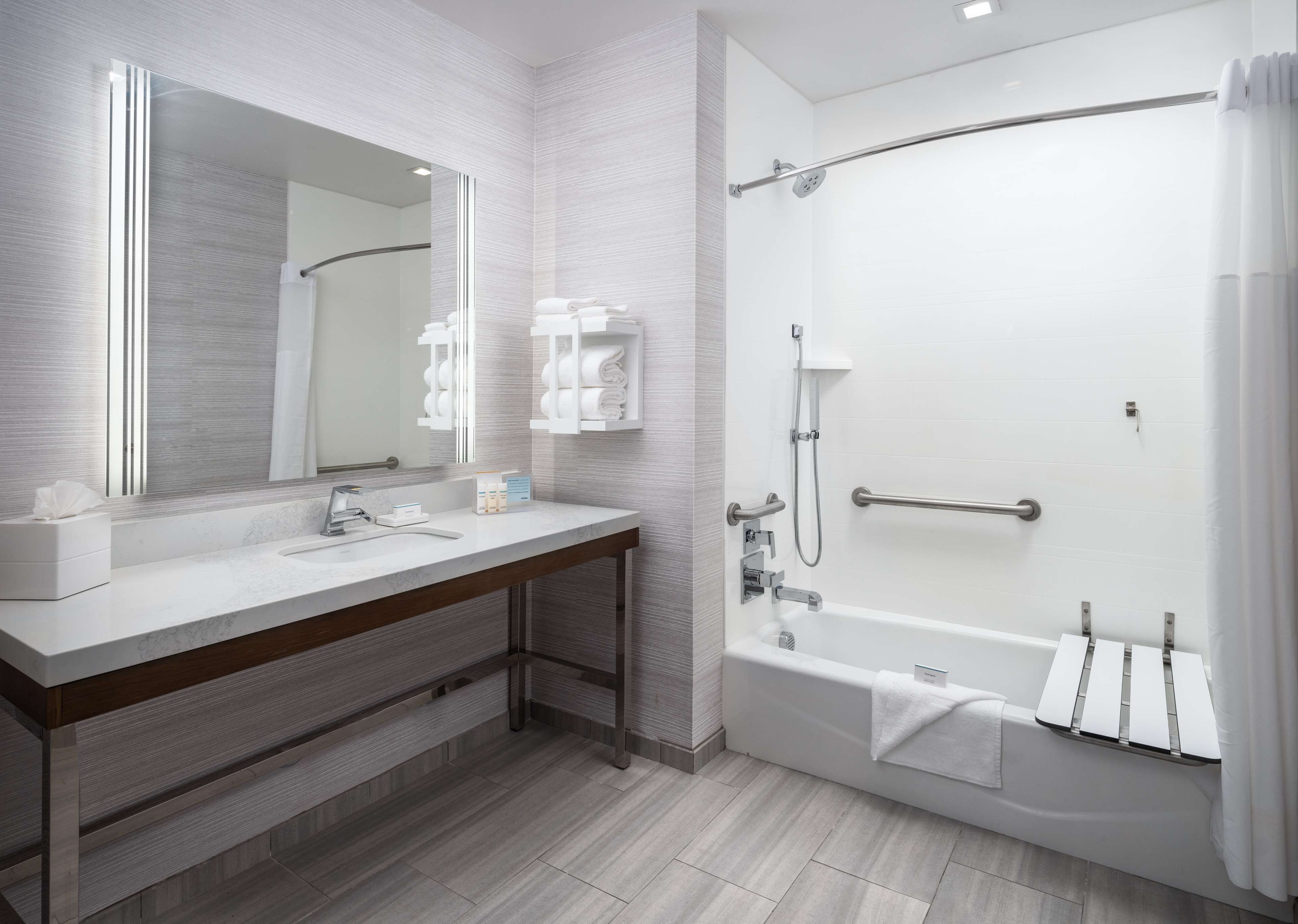 A modern bathroom with a vanity, a large mirror, a shower with a grab bar, and a bathtub.
