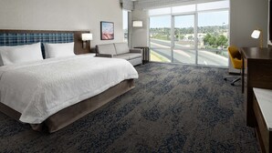 Ein Hotelzimmer mit einem großen Bett, einem Schreibtisch, einem Sessel, einer Couch und einem großen Fenster mit Blick auf die Stadt.