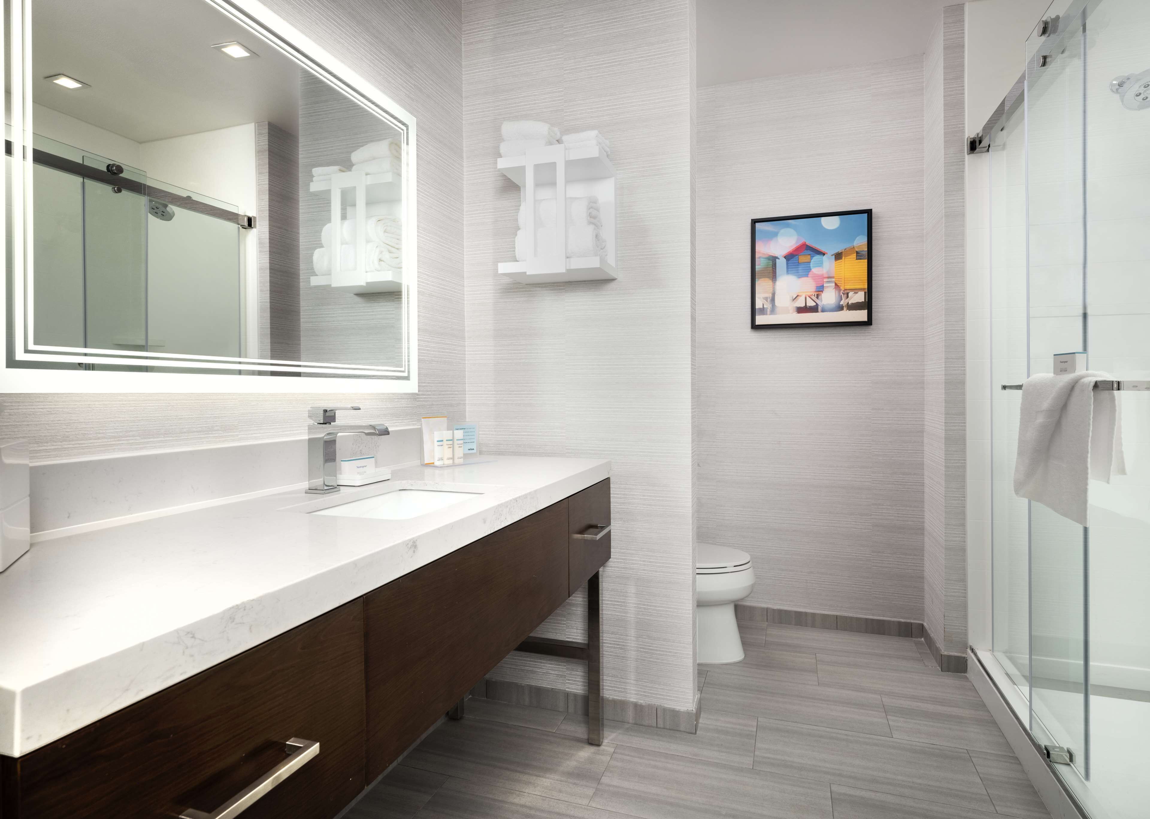 Une salle de bain moderne avec un grand miroir, un meuble-lavabo avec un évier, des toilettes et un espace douche.