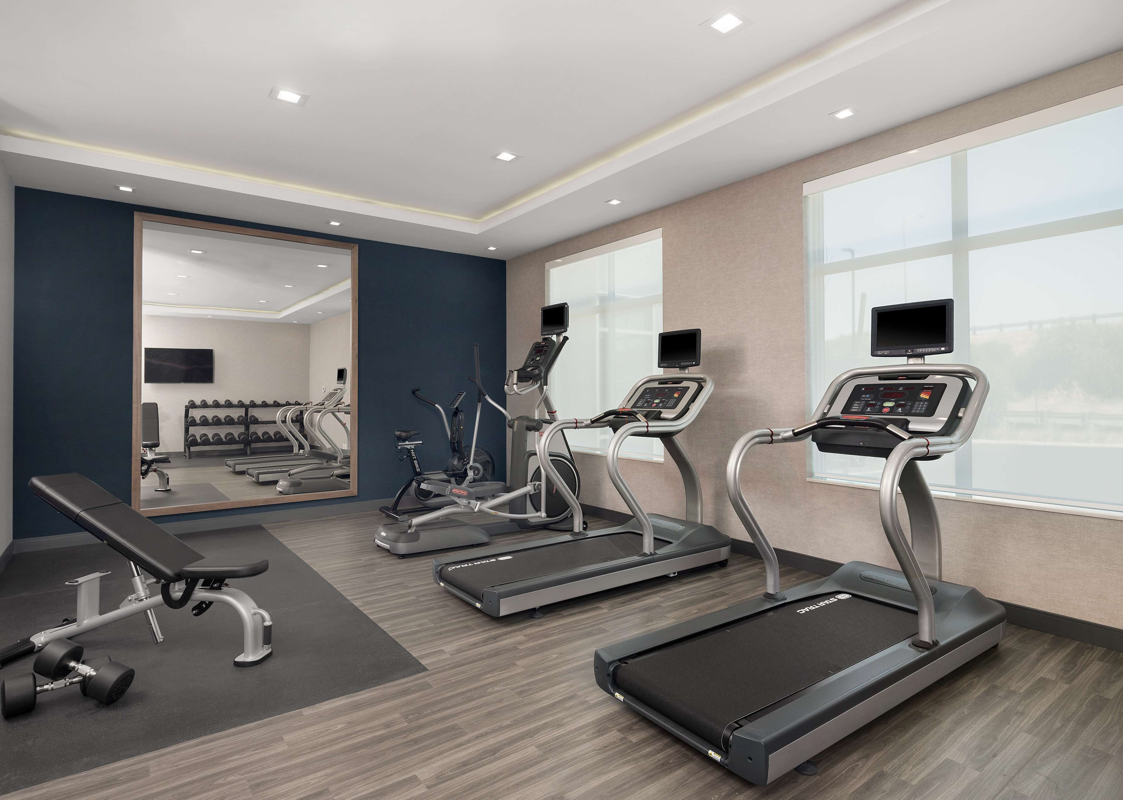 Une salle de sport moderne équipée de tapis de course, d’un banc et d’haltères.