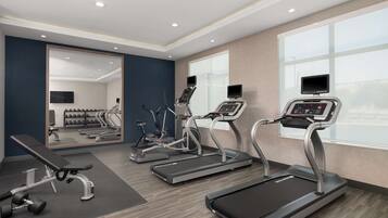 Une salle de sport moderne équipée de tapis de course, d’un banc et d’haltères.