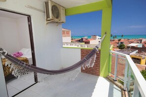 A balcony with a hammock, a view of the sea, and a building with red roofs. - Pousada Verdes Mares (Maragogi)