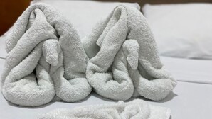 Una cama bien hecha con toallas blancas y dos artículos de aseo en una bolsa de plástico.
