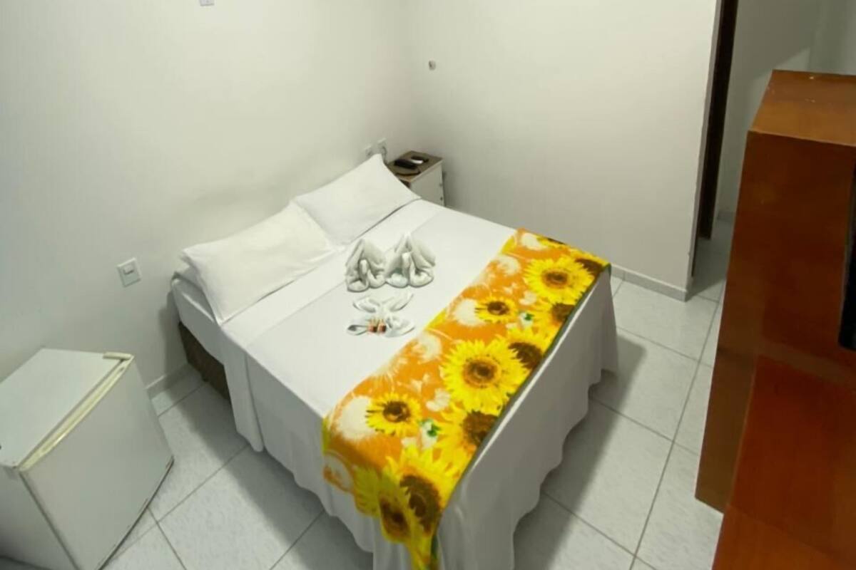 Ein kleiner, sauberer Raum mit einem Bett, einem Nachttisch und einer kleinen, weißen Kommode.