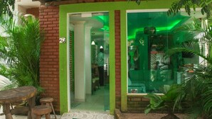 Entrada de un edificio con fachada verde, un cartel con el número 26 y una puerta de cristal que da al interior.