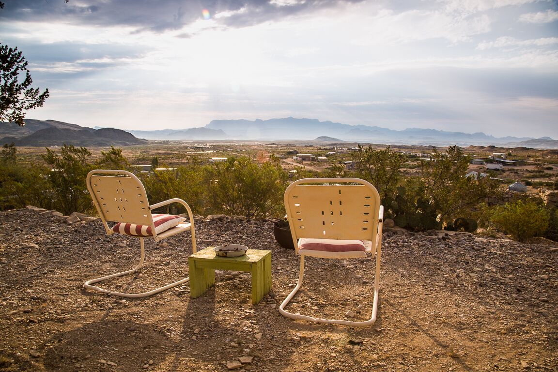 Two rocking chairs on a rocky terrain with a view of distant mountains and a town.