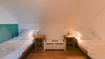 A small, cozy room with two single beds, each with a nightstand and a lamp. There is a white storage box in the center of the room.
