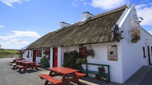 Un bâtiment blanc avec un toit de chaume, une porte rouge et une enseigne publicitaire pour la bière Guinness. Il y a des tables de pique-nique à l'extérieur.