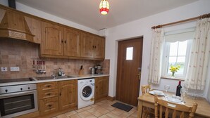 Une cuisine avec des meubles de rangement en bois, un lave-linge, une table à manger avec des chaises et une fenêtre avec des rideaux.