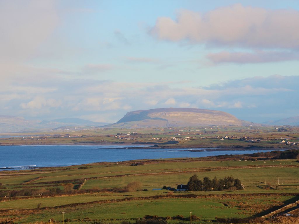 A coastal landscape with rolling hills, a body of water, and scattered houses.