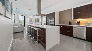 A modern kitchen with a central island, dark wooden cabinets, stainless steel appliances, and a bar stool seating area. - Liberty Holiday: Private Pool, Water Park, Golf View, Near Disney (Kissimmee)