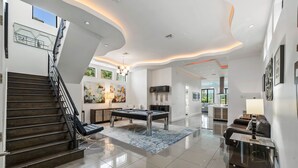 A modern living room with a pool table, a sofa, and a staircase. - Liberty Holiday: Private Pool, Water Park, Golf View, Near Disney (Kissimmee)
