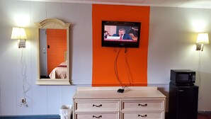 A hotel room with a television mounted on the wall, a dresser, a mirror, and two wall-mounted lamps. - Blue Haven Motel I-75 North Exit 128&129 (Rocky Top)