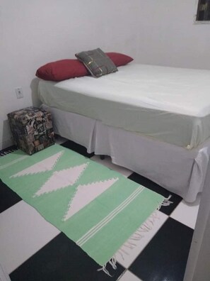 A simple room with a bed, a small storage unit, and a patterned rug.