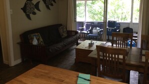 A living room with a wooden sofa, a coffee table, and a dining table with chairs. There is a large window with curtains, and two wall-mounted decorations. - Water access Island Cottage in sheltered cove (South Frontenac Region)