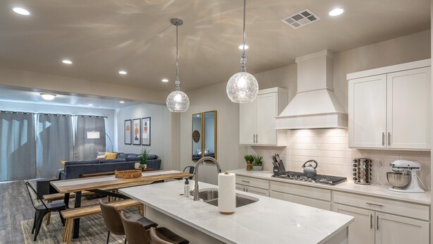 Une cuisine moderne avec des meubles blancs, un îlot central et des luminaires suspendus.