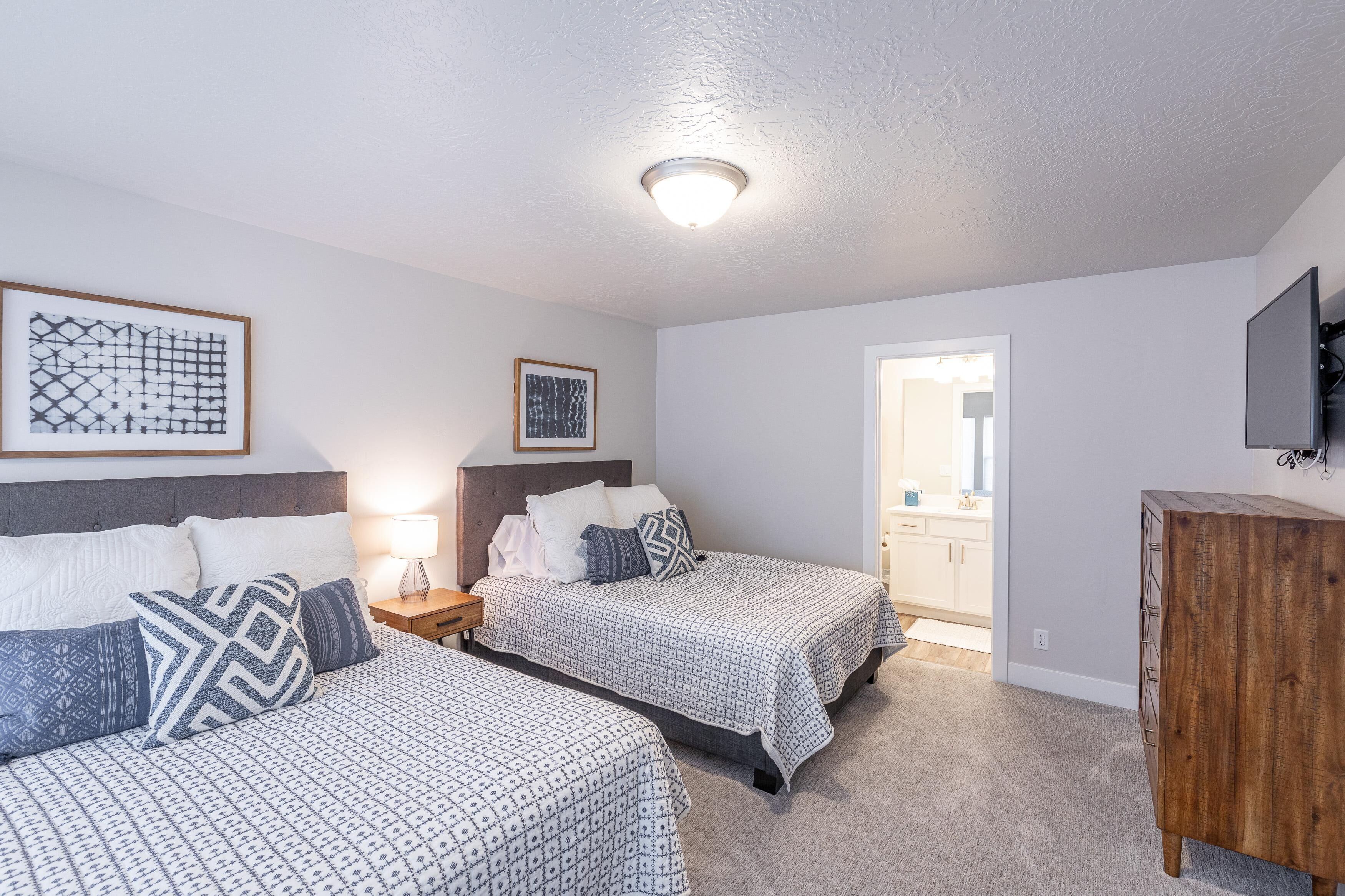 Une chambre avec deux lits, une commode en bois et un téléviseur fixé au mur.