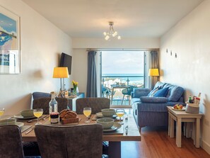 A hotel room with a dining area, a sofa, a TV, and a view of the sea. - 2 bedroom accommodation in Newquay (Newquay)
