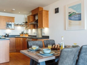 Una cocina moderna con armarios de madera, microondas integrado y comedor con mesa lista para dos personas.