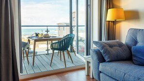 Ein Zimmer mit Balkon, Tisch mit Stühlen, einer Couch und einer Lampe.