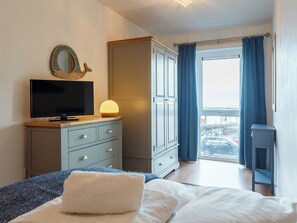 A bedroom with a bed, a dresser, a television, a lamp, and a view through a window. - 2 bedroom accommodation in Newquay (Newquay)