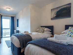 A hotel room with two beds, a large window with curtains, a painting on the wall, and a ceiling light. - 2 bedroom accommodation in Newquay (Newquay)