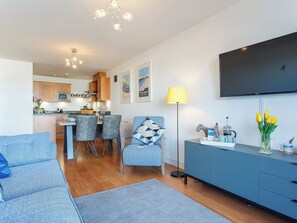 A modern living room with a sofa, a dining area with chairs, a kitchen in the background, a flat-screen TV mounted on the wall, and a lamp. - 2 bedroom accommodation in Newquay (Newquay)