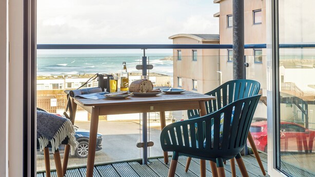 Ein Balkon mit Tisch, Stühlen und Blick auf das Meer.