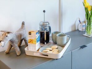 A tray with a coffee maker, two mugs, a box of cookies, and a decorative figurine on a modern kitchen counter. - 2 bedroom accommodation in Newquay (Newquay)